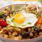 A bowl of food with vegetables, tofu, and a sunny-side-up egg on top, promoting "18 Sheet Pan Dinners That Practically Cook Themselves.