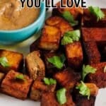 A plate of seasoned, cubed tofu garnished with herbs, served with a bowl of dipping sauce. Text reads, “18 Vegan Recipes You’ll Love.”.