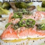 Close-up of baked salmon fillets topped with sliced green chili and capers, surrounded by roasted broccoli on a baking tray. Text on image reads "19 Chili Recipes That Bring the Heat and the Hype.