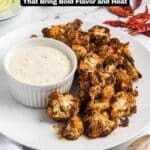 Plate of roasted cauliflower with a bowl of creamy dipping sauce, garnished with dried red chili peppers, and celery slices on the side.