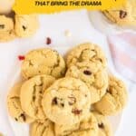 A plate of cranberry cookies sits on a white surface, surrounded by more cookies, a bowl, and a striped napkin. Text reads "20 Cranberry Recipes That Bring the Drama.