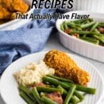 A plate with green beans and bacon, mashed potatoes, and fried chicken sits on a table, with dishes of rice, green beans, and fried chicken in the background. Text reads, "20 Green Bean Recipes That Actually Have Flavor.