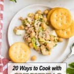 A plate with a chickpea and tuna salad, garnished with green onions, served with two round crackers. Text overlay reads "20 Ways to Cook with Chickpeas Without Getting Bored.