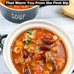 Two bowls of chunky soup with beans, vegetables, and herbs on a white table, with bread and a labeled soup bowl in the background. Text reads "22 Soups That Warm You From the First Sip.