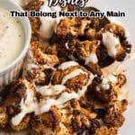 Roasted cauliflower florets topped with white sauce served on a white plate next to a small bowl of creamy dip.