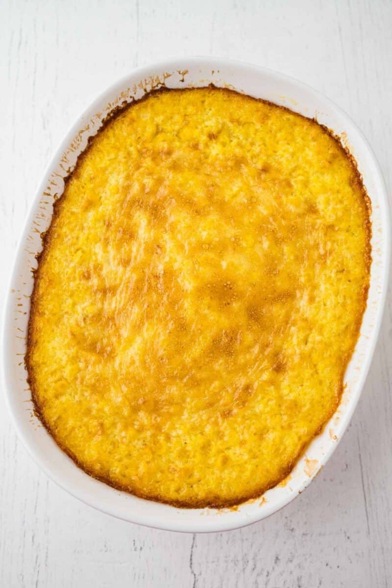 A baked casserole dish filled with a golden-brown cornbread pudding, shown from above on a white surface.