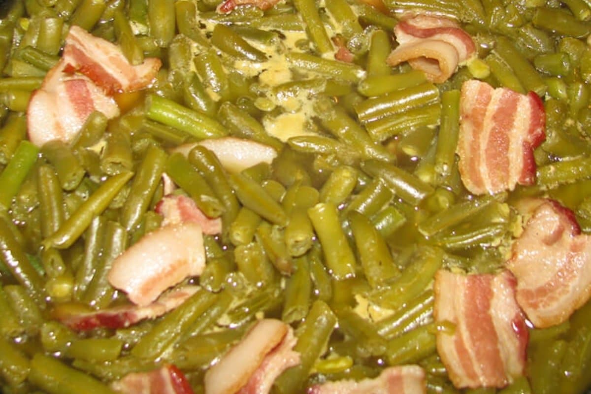 Green beans and strips of bacon cooked together, with visible pieces of bacon distributed among the beans.