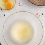 A glass bowl with egg whites, a small bowl with two eggs, and a bowl of chocolate cake mix on a white surface with scattered sprinkles.