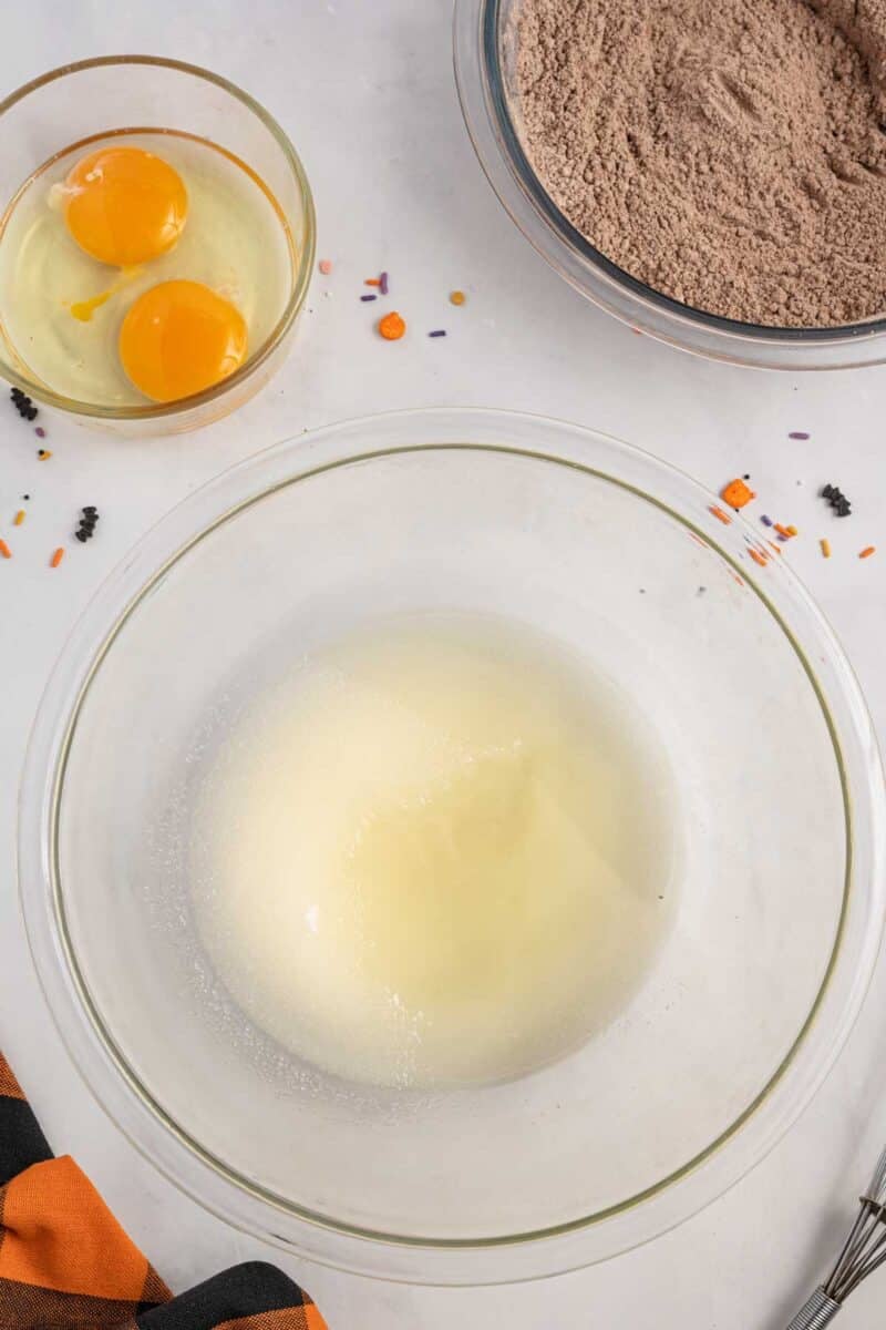 A glass bowl with egg whites, a small bowl with two eggs, and a bowl of chocolate cake mix on a white surface with scattered sprinkles.