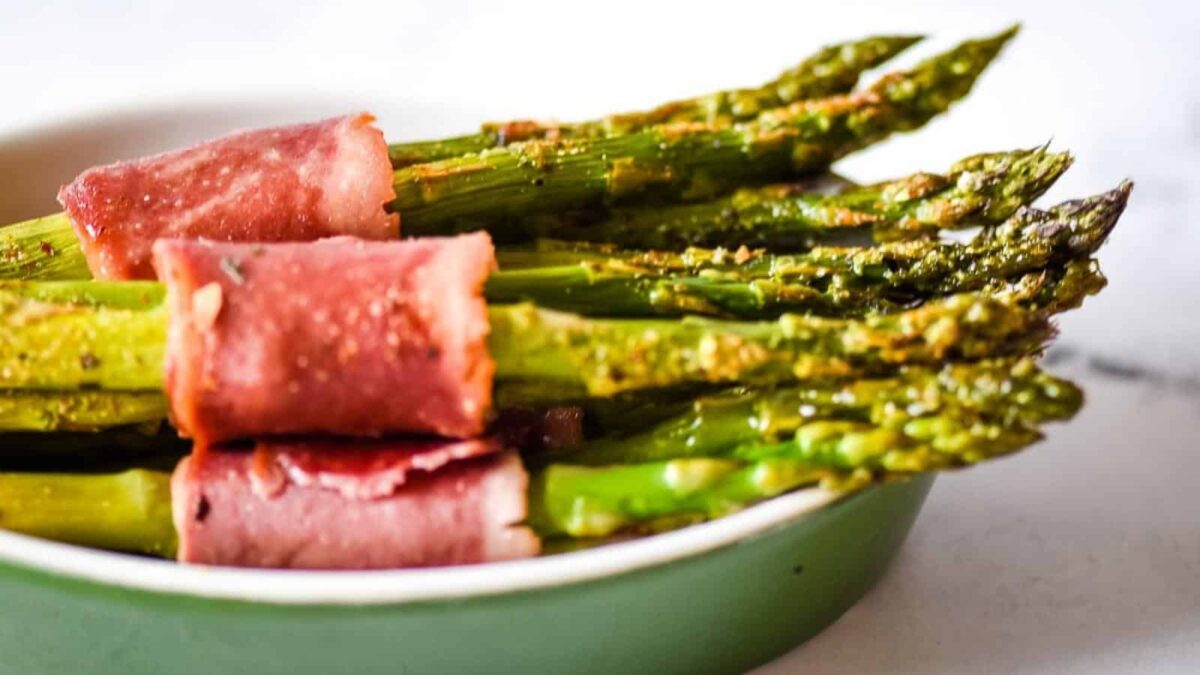 Several spears of asparagus wrapped in slices of ham are arranged in a green dish, perfect for adding to your next party table and inspiring new party recipes.