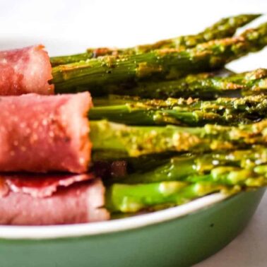 Several spears of asparagus wrapped in slices of ham are arranged in a green dish, perfect for adding to your next party table and inspiring new party recipes.