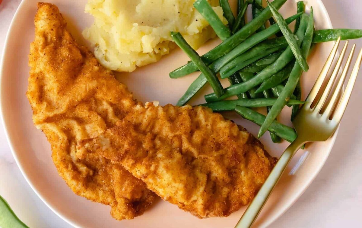 A plate with two breaded chicken tenders, mashed potatoes, green beans, and a gold fork&mdash;perfect for enjoying homemade takeout or trying your hand at copycat dishes.