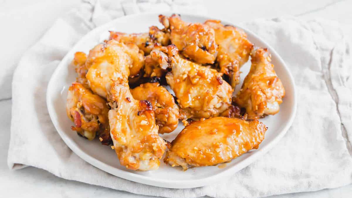 A white plate filled with flavorful glazed chicken wings sits on a light-colored cloth napkin.