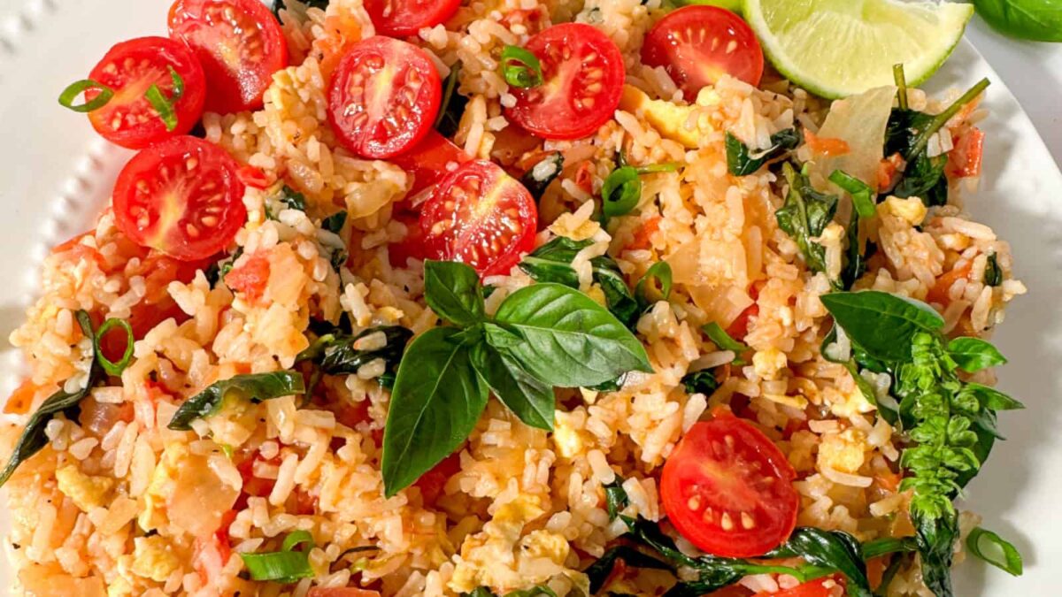 Plate of fried rice with halved cherry tomatoes, scrambled eggs, green onions, spinach, and fresh basil, garnished with lime wedges—a delicious option for fans of Vegetarian Meals and creative Vegetarian Recipes.