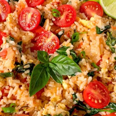 Plate of fried rice with halved cherry tomatoes, scrambled eggs, green onions, spinach, and fresh basil, garnished with lime wedges—a delicious option for fans of Vegetarian Meals and creative Vegetarian Recipes.