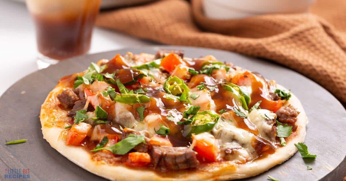 A personal-sized strong toppings pizza topped with diced tomatoes, green peppers, beef, cheese, fresh herbs, and a drizzle of barbecue sauce on a dark round serving board.