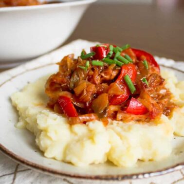 A plate of mashed potatoes topped with a vegetable stew and garnished with chopped chives showcases the old-world flavor of European cuisine, served on a white patterned napkin.