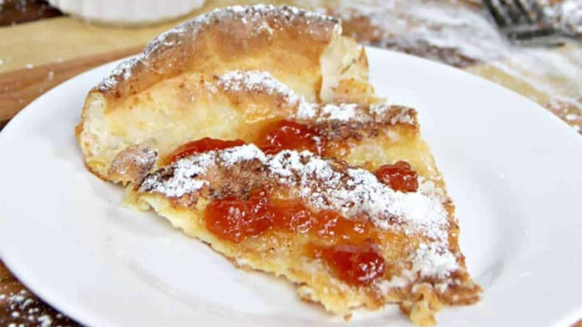A slice of baked pancake topped with powdered sugar and fruit preserves is served on a white plate, making it a breakfast feast to remember.