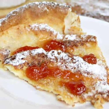 A slice of baked pancake topped with powdered sugar and fruit preserves is served on a white plate, making it a breakfast feast to remember.