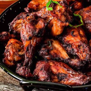 A black bowl filled with grilled or roasted chicken wings, an enticing example of interesting chicken recipes, garnished with fresh herbs and set on a rustic wooden surface.