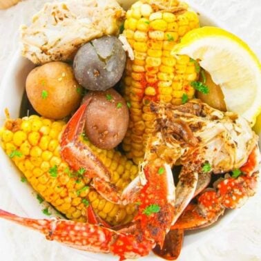 A bowl containing crab legs, corn on the cob, potatoes, and a lemon wedge, garnished with parsley—a perfect choice for Instant Pot dinners and easy dinner recipes.