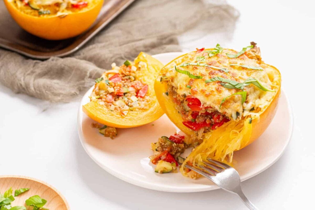 A baked spaghetti squash half stuffed with vegetables and cheese sits on a white plate, highlighting how light recipes can be both satisfying and delicious, with a fork and some flavorful filling spilled onto the plate.