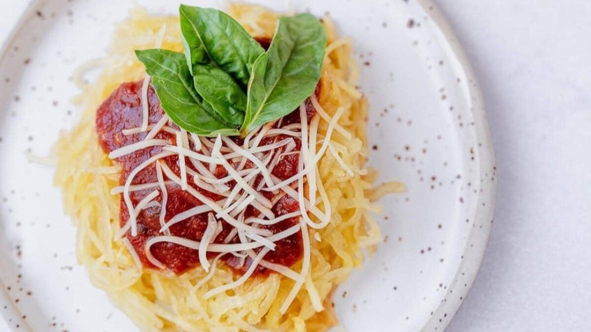 A plate of spaghetti squash topped with marinara sauce, shredded cheese, and fresh basil leaves, served on a speckled white plate—perfect for fans of light recipes.