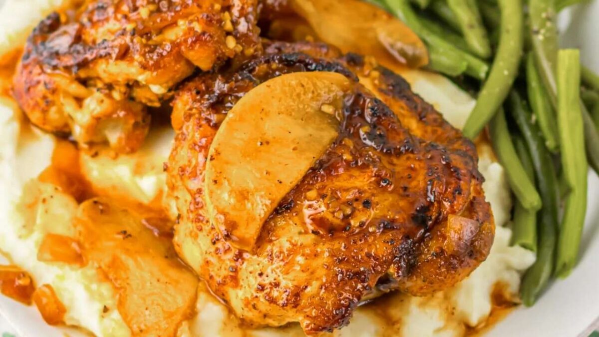Grilled chicken thighs topped with apple slices are served over mashed potatoes with a side of green beans—perfect for easy recipes and a flavorful weeknight dinner.