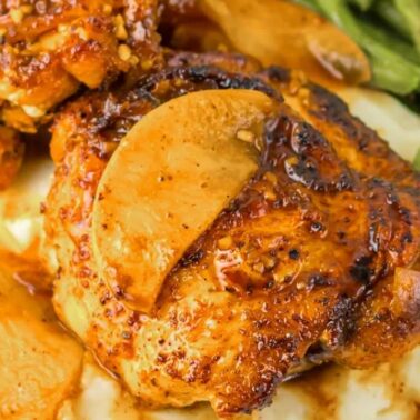 Grilled chicken thighs topped with apple slices are served over mashed potatoes with a side of green beans—perfect for easy recipes and a flavorful weeknight dinner.