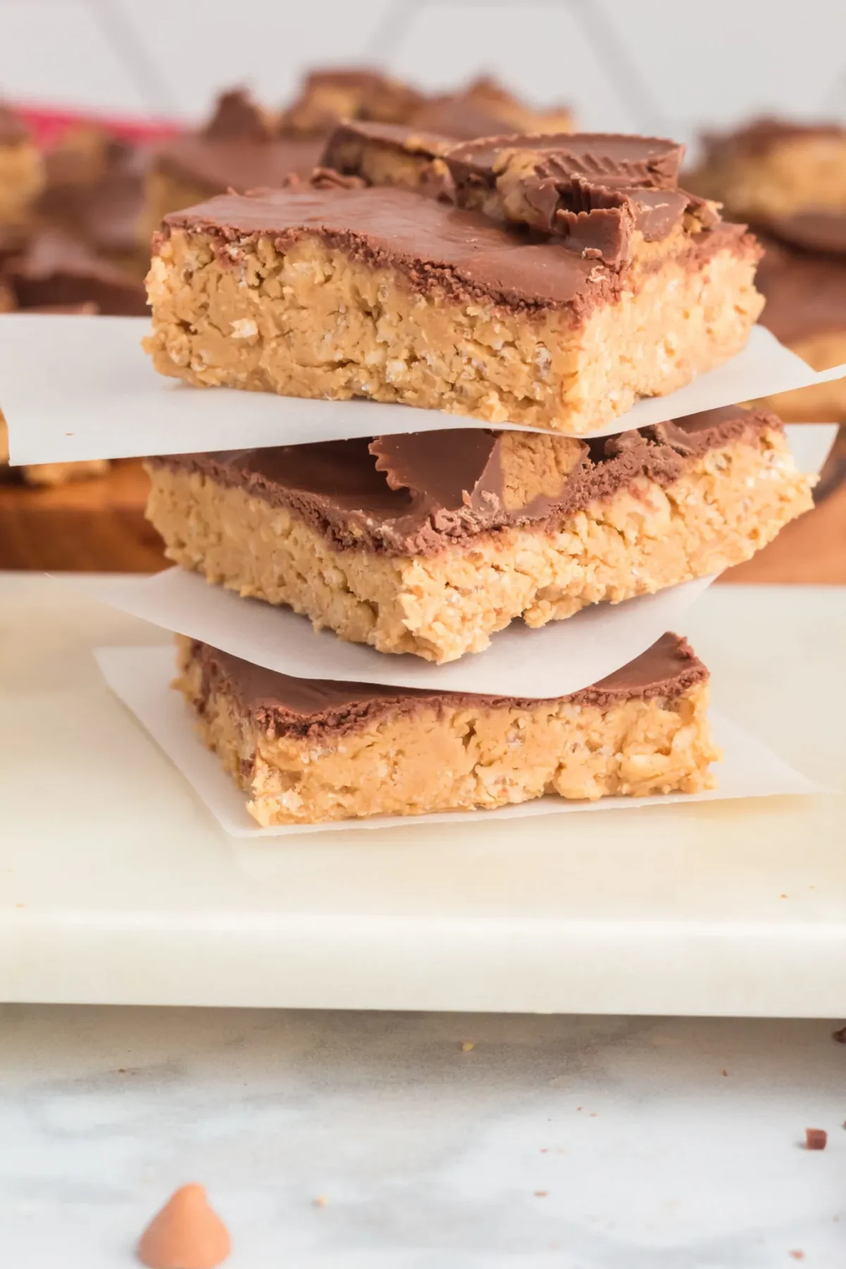 Three peanut butter chocolate bars are stacked on parchment paper on a white surface, making them a perfect treat for fans of chocolate desserts.