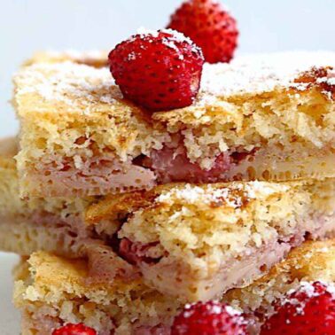 Three stacked slices of strawberry cake with a dusting of powdered sugar, topped and garnished with whole strawberries—perfect alongside your favorite coffee drinks.