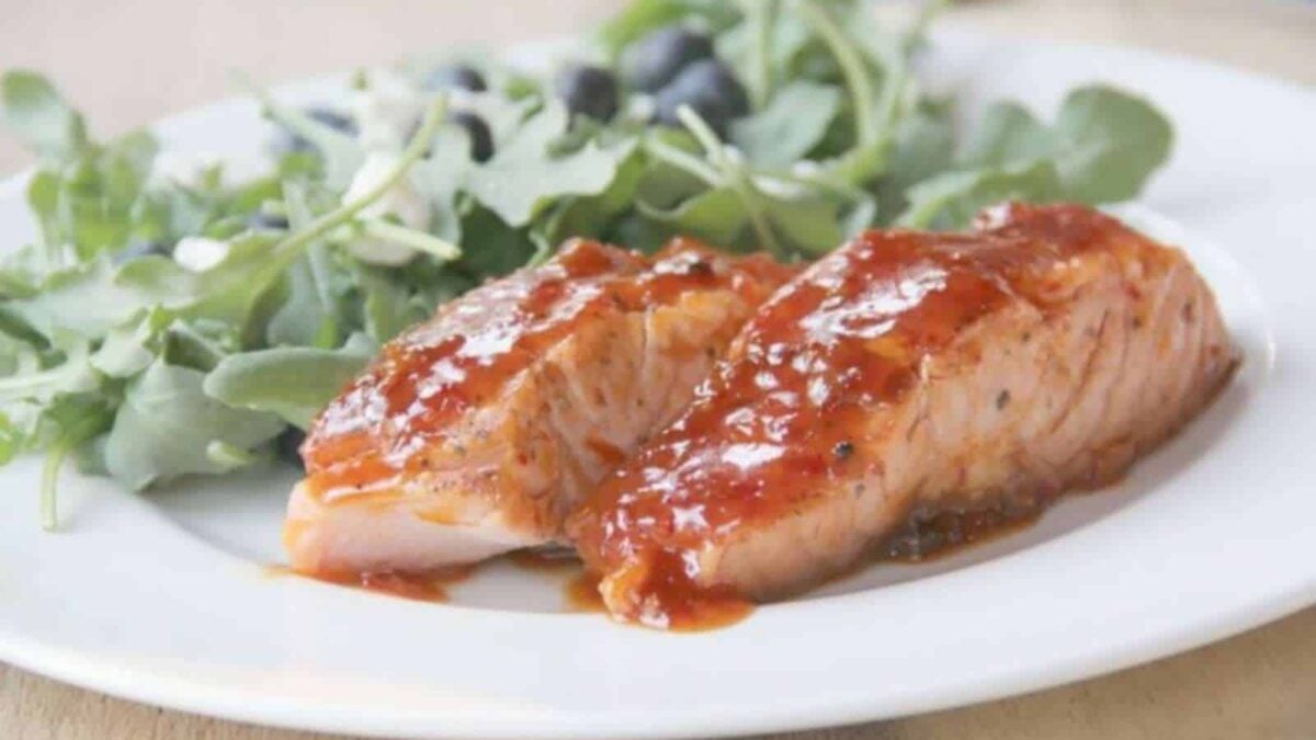 Two pieces of glazed salmon, a highlight of seafood dinners, served with a side of fresh arugula leaves on a white plate.