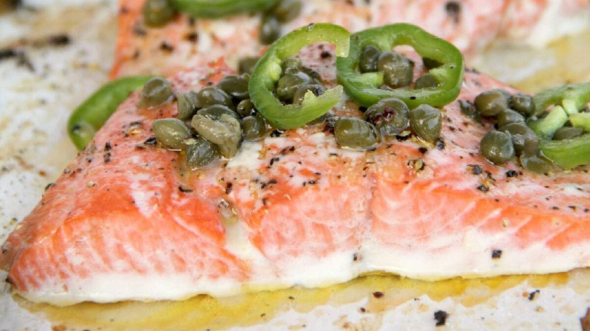 Close-up of cooked salmon filet topped with sliced green peppers, capers, black pepper, and oil—perfect for seafood dinners or those seeking new dinner ideas.