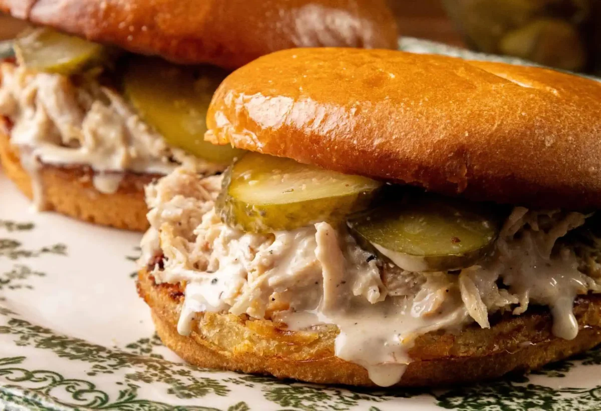 Two chicken sandwiches with shredded chicken, pickles, and white sauce on toasted buns, served on a decorative plate—perfect sandwich meals for quick lunch ideas.