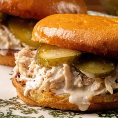 Two chicken sandwiches with shredded chicken, pickles, and white sauce on toasted buns, served on a decorative plate—perfect sandwich meals for quick lunch ideas.