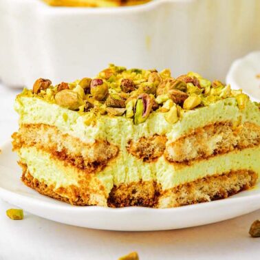 A slice of pistachio tiramisu on a white plate, showing layers of cream, ladyfingers, and chopped pistachios on top—one of the most irresistible no-bake desserts for easy desserts lovers.