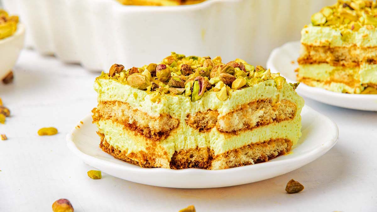 A slice of pistachio tiramisu on a white plate, showing layers of cream, ladyfingers, and chopped pistachios on top—one of the most irresistible no-bake desserts for easy desserts lovers.
