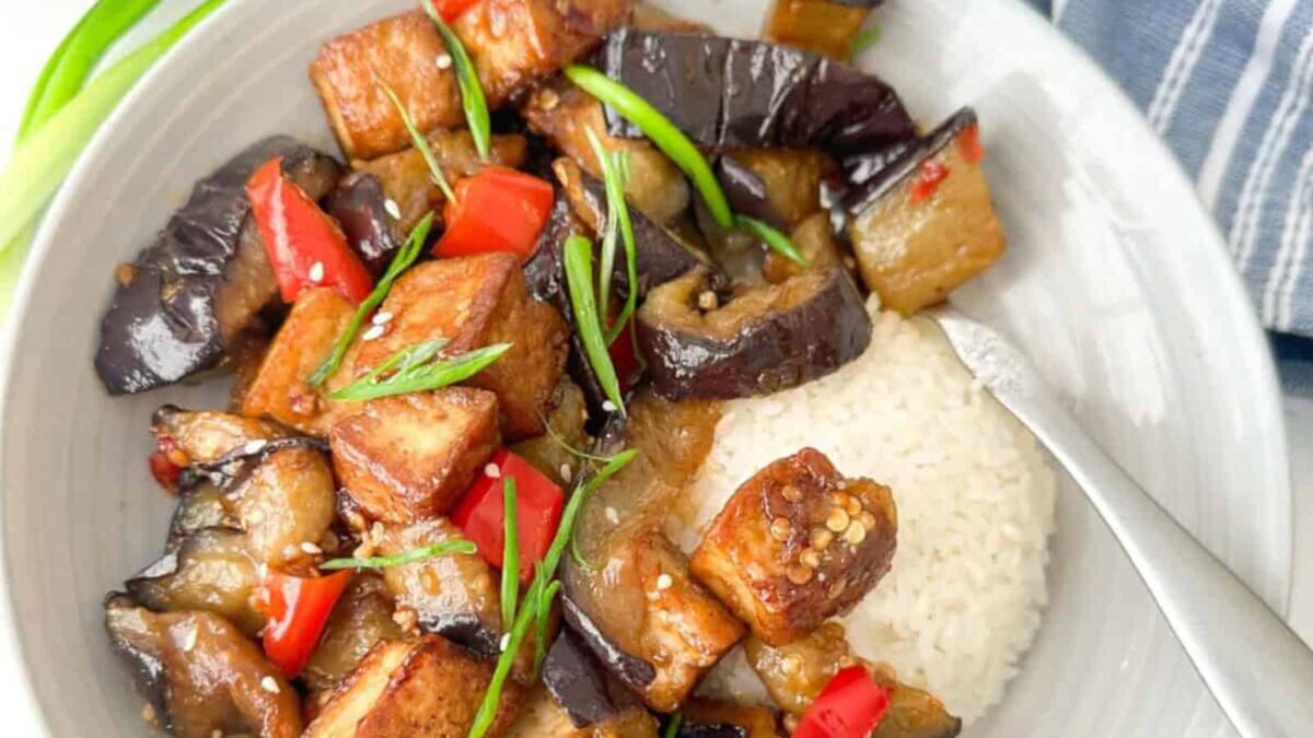 A bowl of white rice topped with stir-fried tofu, eggplant, red bell peppers, and green onions—perfect for fans of delicious eggplant dishes and easy dinner recipes.