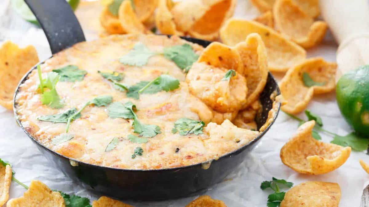 A skillet filled with cheesy dip topped with cilantro sits surrounded by corn chips, with some chips dipped into the cheese—perfect for lovers of easy cheesy meals.