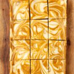 Nine marbled orange and white cheesecake bars are arranged in a 3x3 grid on a wooden surface.