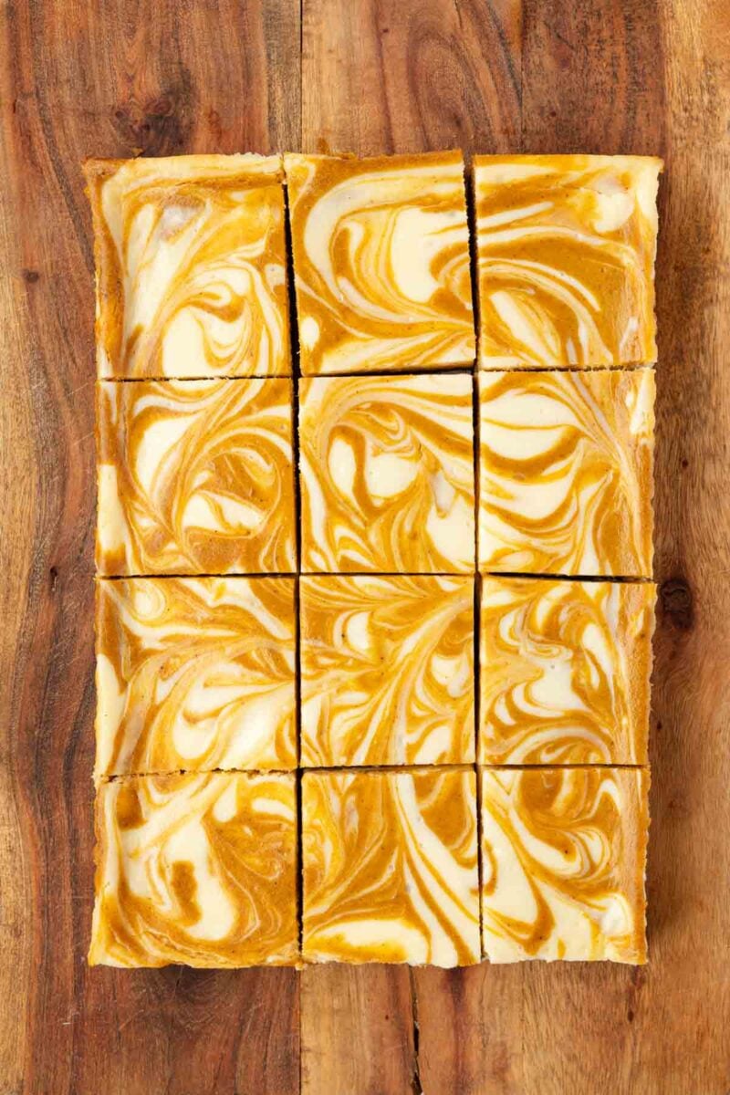 Nine marbled orange and white cheesecake bars are arranged in a 3x3 grid on a wooden surface.