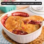 A baked fruit cobbler in a white dish with a serving spoon lifting a portion; fresh strawberries are placed nearby on a woven mat.