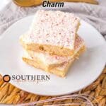Three frosted peppermint dessert bars stacked on a white plate, with a whisk and woven placemat in the foreground. Text above reads, "10 Recipes That Celebrate Peppermint’s Bright Holiday Charm.