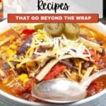 A bowl of tortilla soup topped with shredded cheese, tortilla strips, and jalapeño slices, with a spoon resting on the side of the bowl.