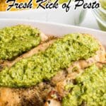 Grilled chicken breasts topped with a generous layer of green pesto sauce, served in a white dish with a lime wedge in the background.