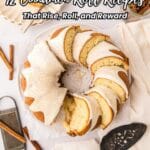A sliced cinnamon roll bundt cake with white icing is displayed on a white table with serving utensils and cinnamon sticks. Text reads: "12 Cinnamon Roll Recipes That Rise, Roll, and Reward.