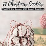 A stack of powdered sugar-coated chocolate crinkle cookies tied with red and white string, with holiday decor in the background. Text reads “14 Christmas Cookies That Fill the Season With Sweet Tradition.”.