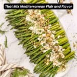 Platter of asparagus topped with crumbled feta cheese, nuts, and herbs, surrounded by scattered dill, pistachios, and a striped cloth. Text reads: "14 Feta Recipes That Mix Mediterranean Flair and Flavor.
