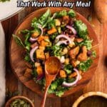 A wooden bowl of salad with roasted sweet potatoes, red onions, greens, and dressing, surrounded by salad ingredients and a wooden spoon.