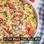 A bowl of pasta salad with rotini, bacon, shredded cheese, tomatoes, and herbs offers a satisfying full meal. It sits on a white surface beside a striped cloth napkin, ready to enjoy while the ingredients stay crisp.
